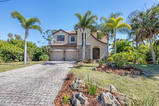 mediterranean / spanish-style home with a garage, stone siding, decorative driveway, a front lawn, and stucco siding