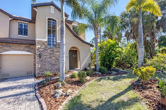 mediterranean / spanish house featuring decorative driveway, stone siding, an attached garage, and stucco siding