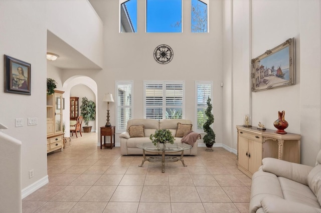 living area with arched walkways, a towering ceiling, baseboards, and light tile patterned floors