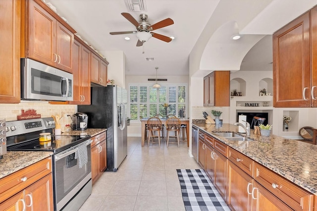 kitchen with brown cabinetry, light tile patterned floors, stainless steel appliances, and a sink