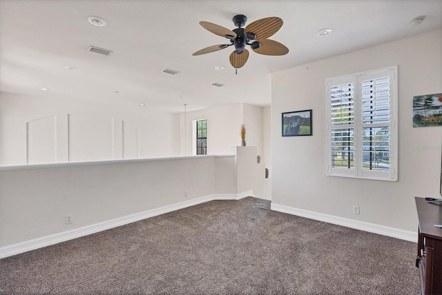 empty room with dark colored carpet, a ceiling fan, visible vents, and baseboards