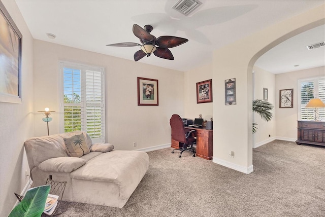 carpeted home office with arched walkways, ceiling fan, visible vents, and baseboards