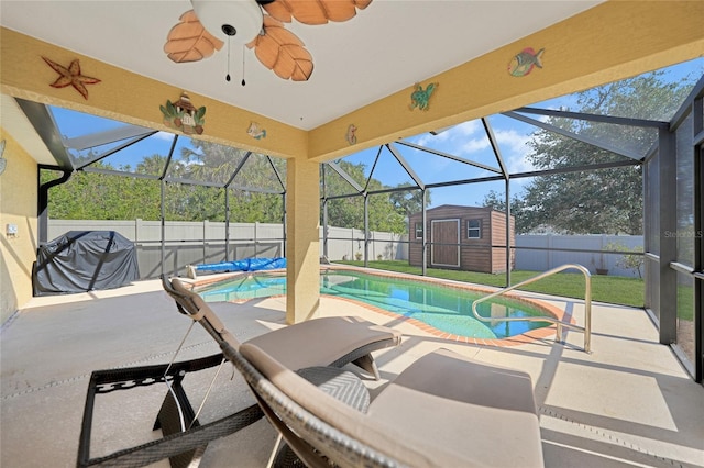 view of swimming pool featuring a storage shed, glass enclosure, a lawn, ceiling fan, and a patio