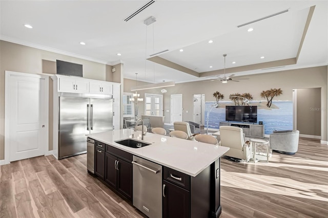 kitchen featuring sink, hanging light fixtures, appliances with stainless steel finishes, a raised ceiling, and a kitchen island with sink