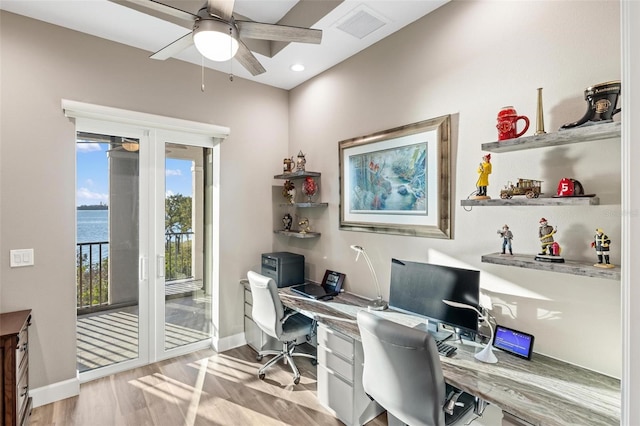 home office with ceiling fan, a water view, and light hardwood / wood-style floors