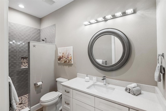 bathroom featuring vanity, toilet, and a tile shower