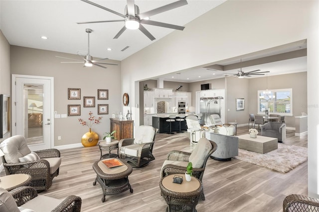 living room featuring ceiling fan, light hardwood / wood-style floors, and a towering ceiling