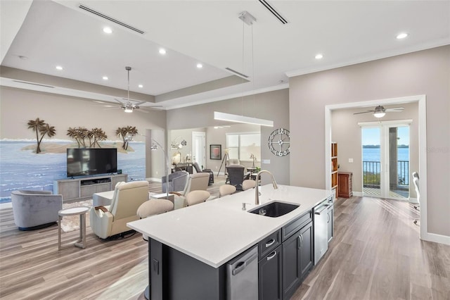 kitchen with light wood-type flooring, sink, a center island with sink, and a water view