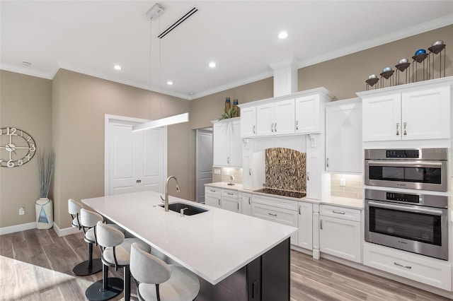 kitchen featuring sink, ornamental molding, an island with sink, decorative backsplash, and white cabinets