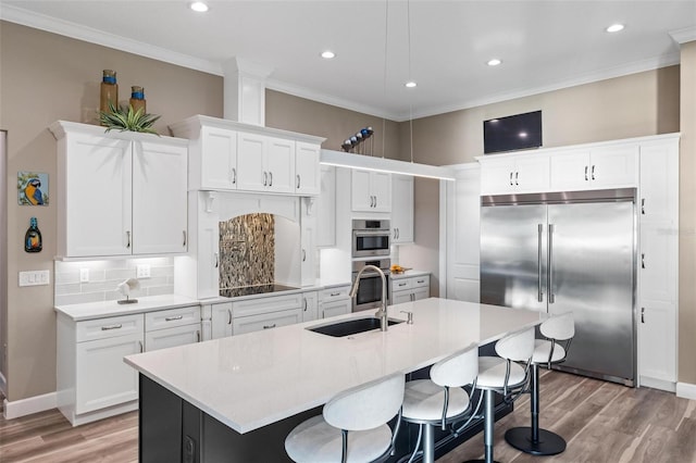 kitchen featuring stainless steel appliances, sink, a center island with sink, and white cabinets