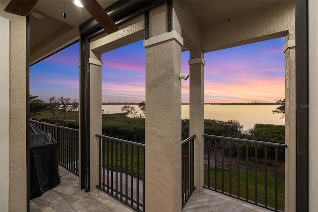 balcony at dusk featuring a water view