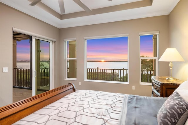 bedroom featuring a water view, a tray ceiling, and access to outside