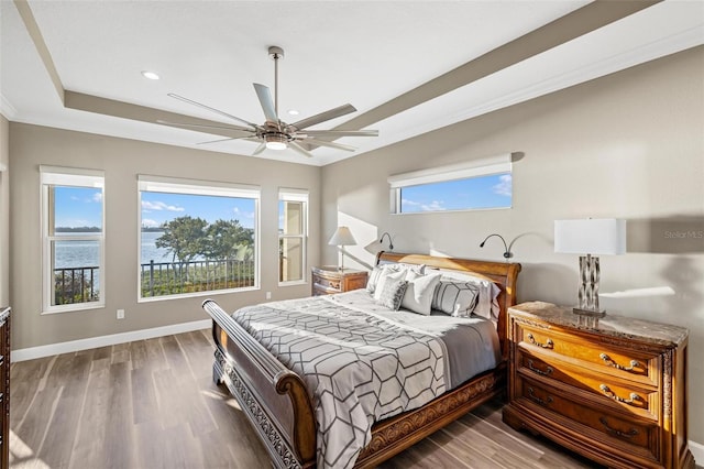 bedroom with a raised ceiling, wood-type flooring, a water view, and ceiling fan