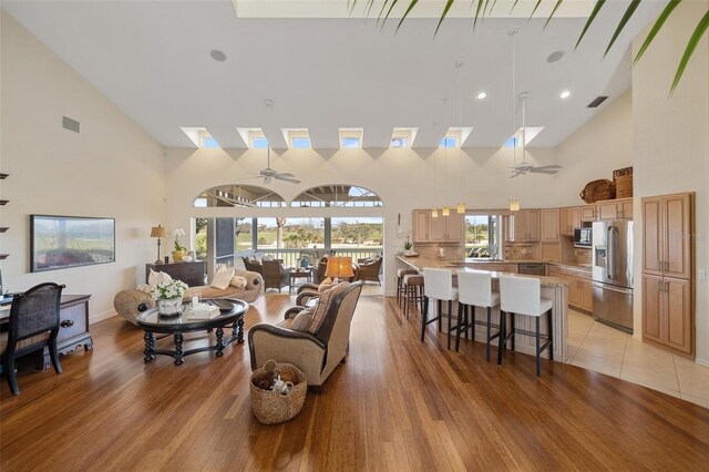 living room featuring high vaulted ceiling, ceiling fan, and light wood-type flooring