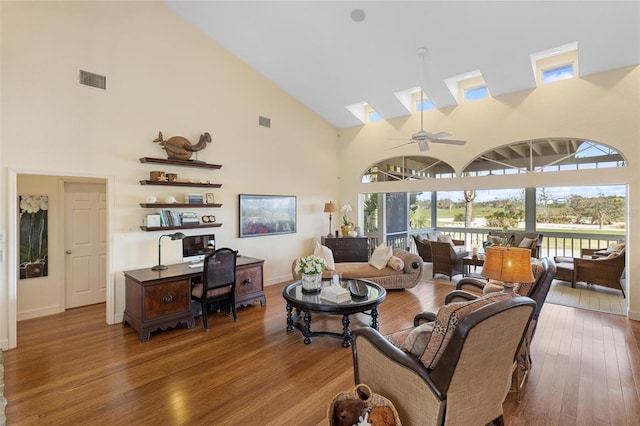 living room with hardwood / wood-style flooring, ceiling fan, a skylight, and high vaulted ceiling