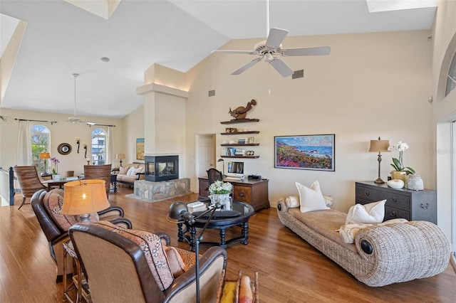 living room with wood-type flooring, high vaulted ceiling, ceiling fan, and a multi sided fireplace