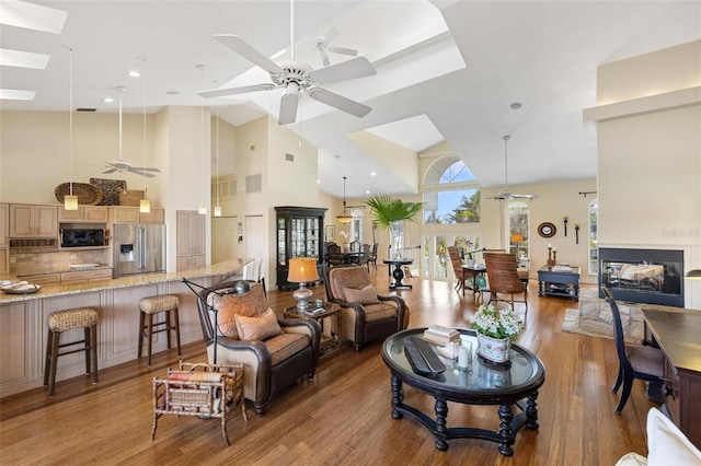 living room featuring hardwood / wood-style flooring, a multi sided fireplace, ceiling fan, and a skylight