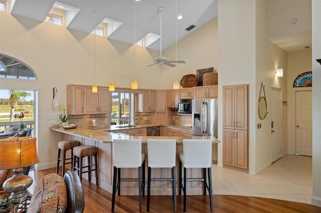 kitchen with appliances with stainless steel finishes, a kitchen breakfast bar, kitchen peninsula, light hardwood / wood-style floors, and backsplash