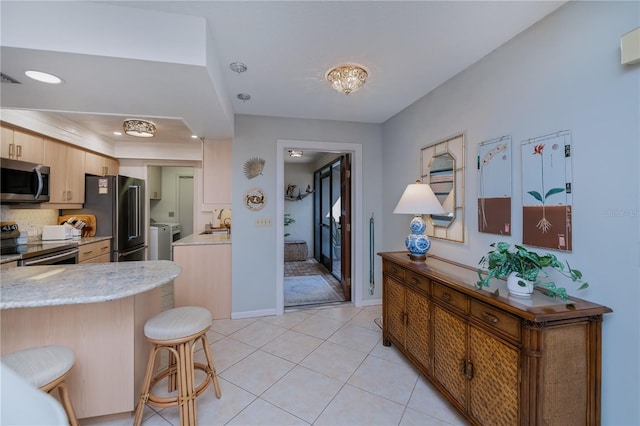 kitchen with a breakfast bar, light tile patterned floors, kitchen peninsula, stainless steel appliances, and washer and clothes dryer