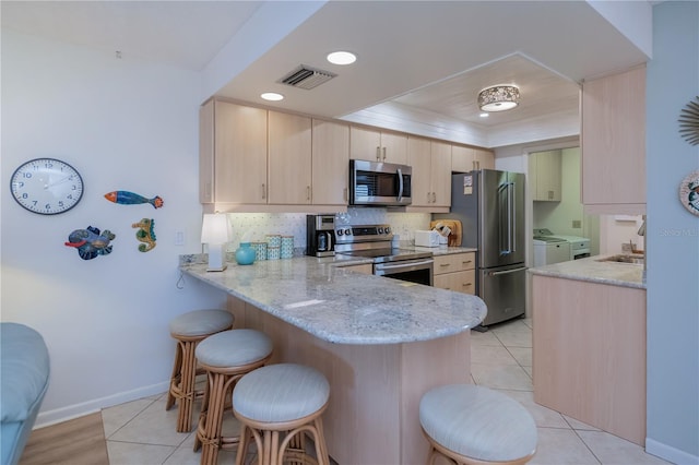 kitchen featuring stainless steel appliances, kitchen peninsula, washing machine and dryer, and light brown cabinets