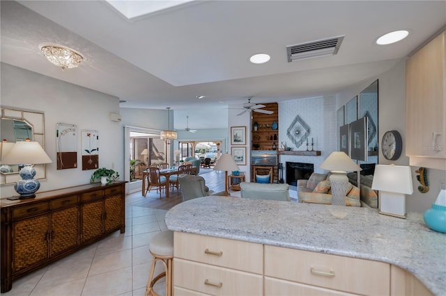 kitchen featuring light stone counters, hanging light fixtures, a fireplace, and light brown cabinets