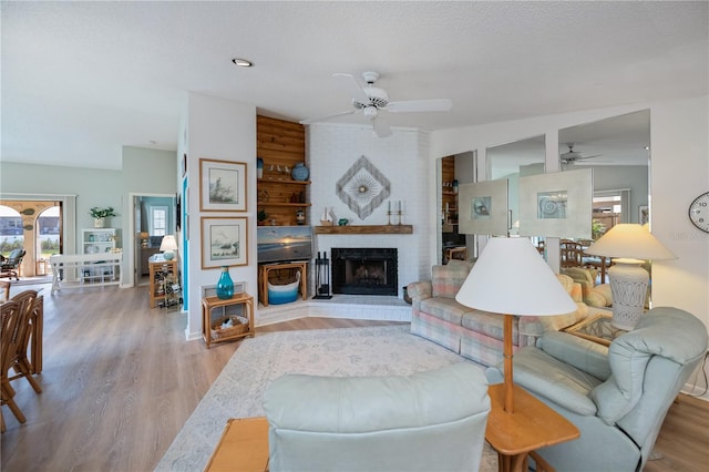 living room with ceiling fan, a fireplace, and light hardwood / wood-style flooring