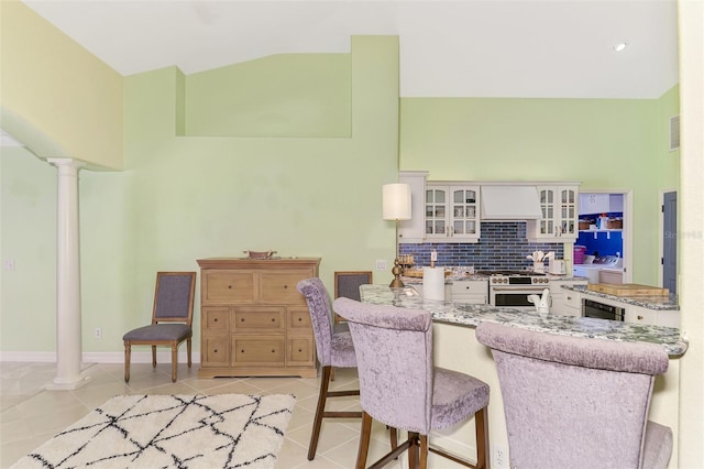 kitchen with premium range hood, decorative columns, tasteful backsplash, white cabinets, and light tile patterned floors