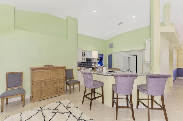 kitchen featuring white cabinetry, light stone counters, high end refrigerator, light tile patterned floors, and kitchen peninsula