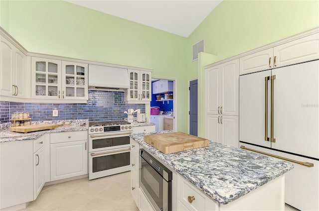 kitchen featuring independent washer and dryer, built in appliances, light stone counters, tasteful backsplash, and white cabinets