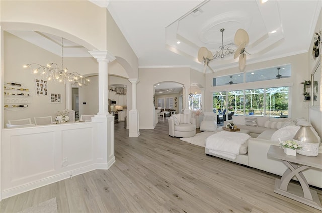 living room featuring crown molding, a raised ceiling, light hardwood / wood-style floors, and ornate columns