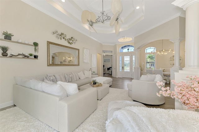 living room featuring decorative columns, crown molding, a chandelier, a tray ceiling, and light hardwood / wood-style floors