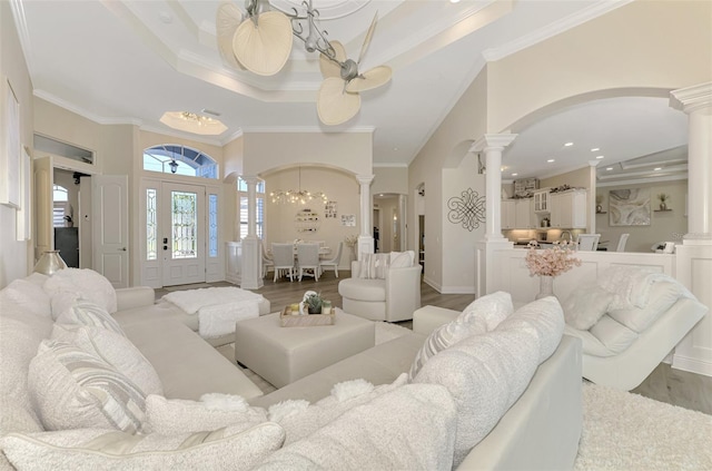 living room featuring a towering ceiling, decorative columns, ornamental molding, a tray ceiling, and light hardwood / wood-style flooring