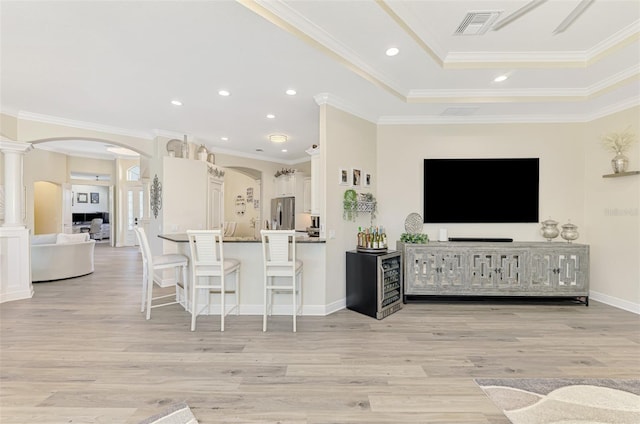 interior space with ornate columns, ornamental molding, a tray ceiling, and light hardwood / wood-style flooring