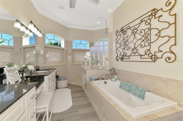 bathroom with crown molding, wood-type flooring, a relaxing tiled tub, and vanity