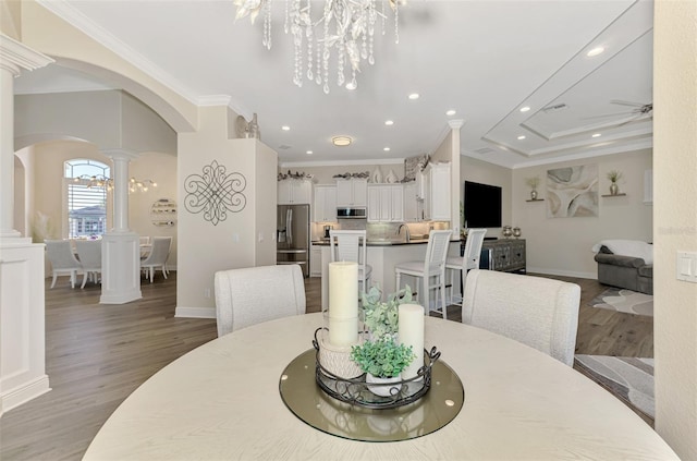 dining room featuring ornate columns, ornamental molding, ceiling fan with notable chandelier, and light wood-type flooring