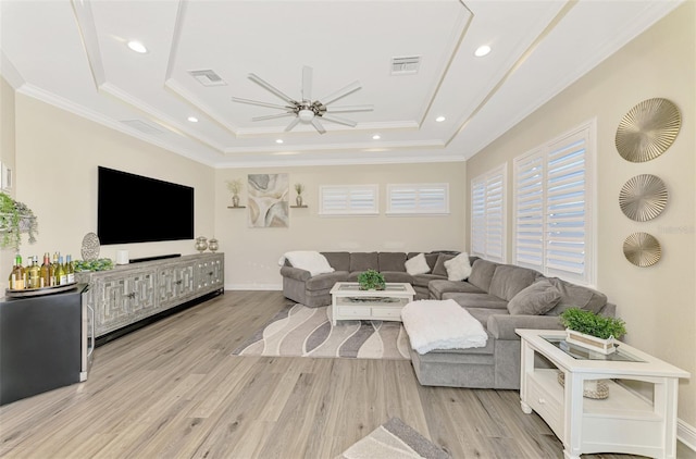 living room featuring crown molding, a raised ceiling, ceiling fan, and light wood-type flooring