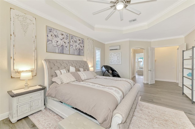 bedroom with a tray ceiling, ceiling fan, light hardwood / wood-style floors, crown molding, and a wall unit AC