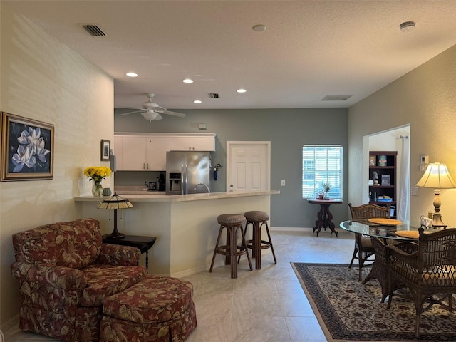 kitchen featuring a breakfast bar area, white cabinetry, stainless steel fridge, kitchen peninsula, and ceiling fan