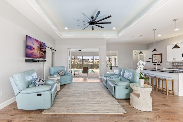 living room with a raised ceiling, a barn door, ceiling fan, and light hardwood / wood-style flooring