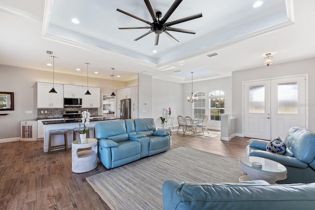 living room featuring a tray ceiling, ceiling fan with notable chandelier, dark hardwood / wood-style floors, and french doors