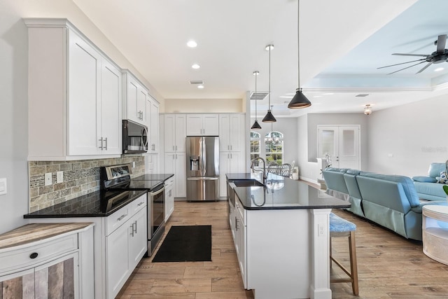 kitchen featuring pendant lighting, appliances with stainless steel finishes, white cabinetry, backsplash, and an island with sink