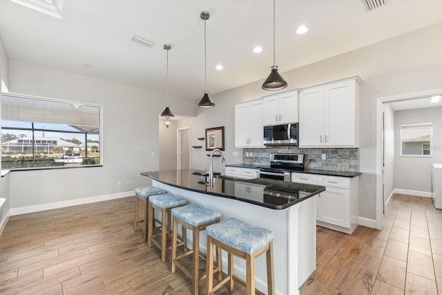 kitchen featuring sink, a breakfast bar, appliances with stainless steel finishes, a kitchen island with sink, and white cabinetry