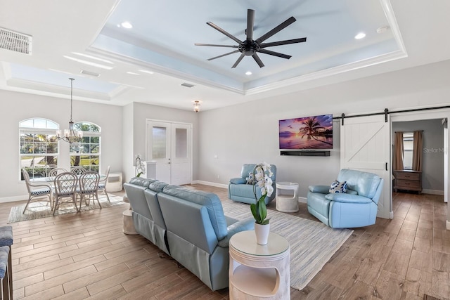 living room with a tray ceiling, a barn door, wood finished floors, and visible vents