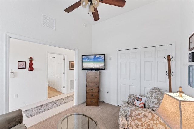 carpeted living room featuring a towering ceiling and ceiling fan