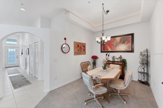 dining area with an inviting chandelier, a tray ceiling, and light tile patterned flooring