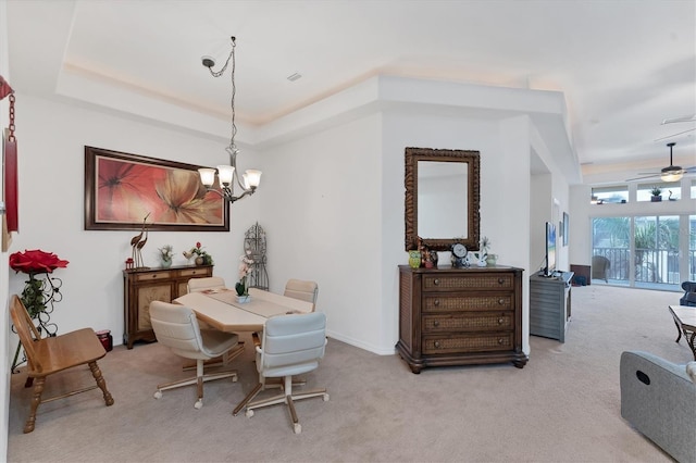 dining space featuring a tray ceiling, ceiling fan with notable chandelier, and light colored carpet