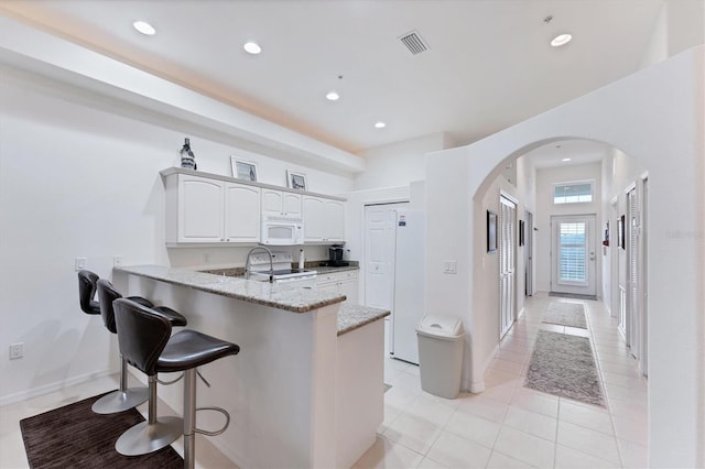 kitchen with white appliances, white cabinetry, light stone countertops, light tile patterned flooring, and kitchen peninsula