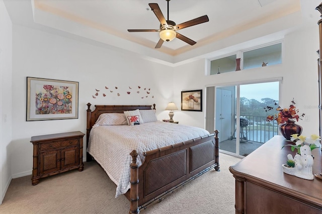 carpeted bedroom featuring access to exterior, ceiling fan, and a tray ceiling