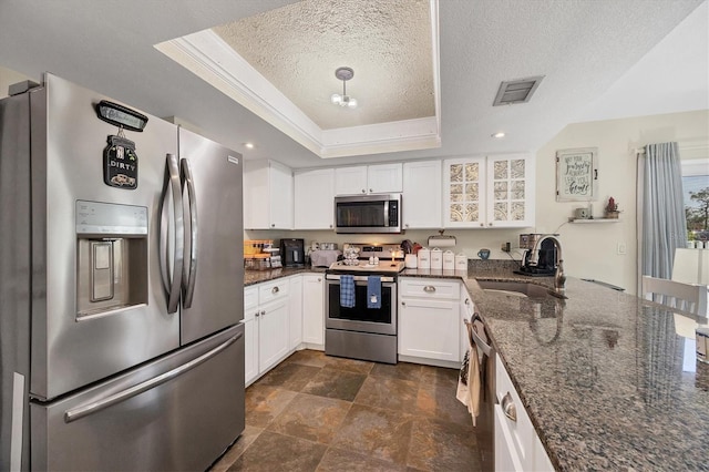 kitchen with sink, appliances with stainless steel finishes, a raised ceiling, dark stone counters, and white cabinets