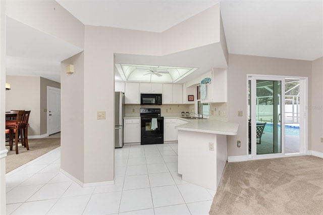 kitchen featuring black appliances, light carpet, kitchen peninsula, a raised ceiling, and white cabinets